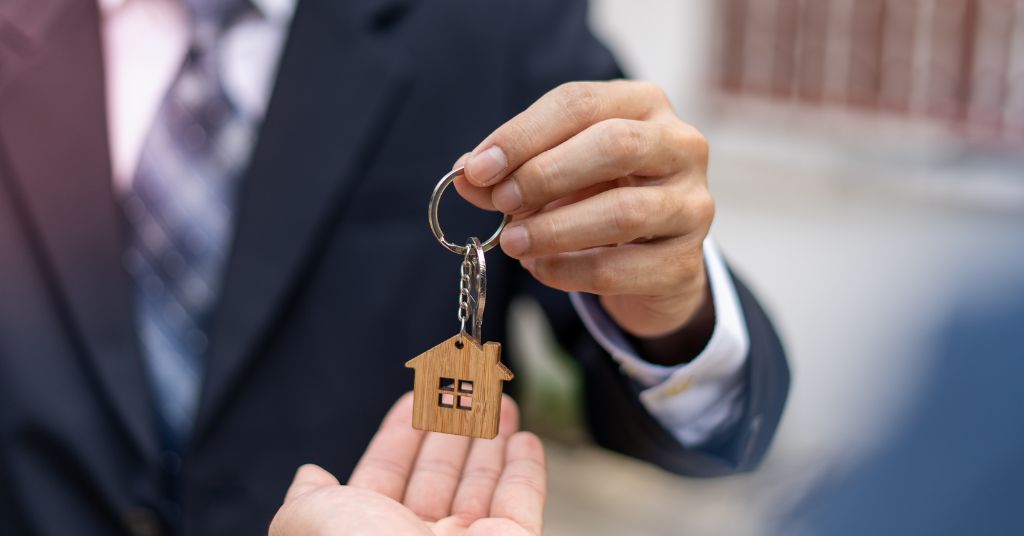 Professional handing wooden house keychain - real estate agent or broker transfer moment