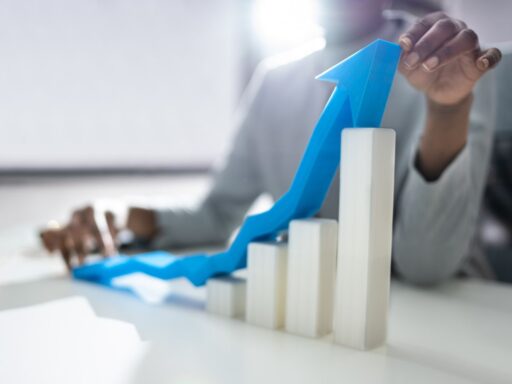 Business graph showing upward trend with blue arrow over white ascending bar chart.